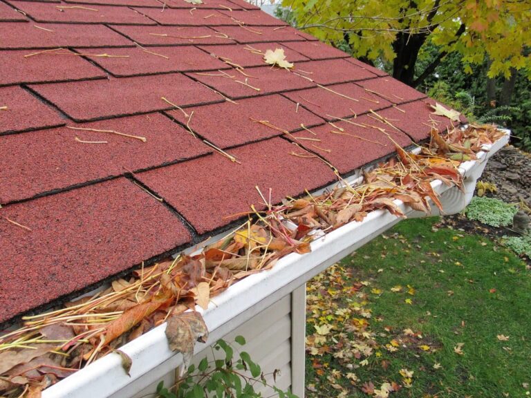 Clogged gutters filled with fallen leaves on a house roof.